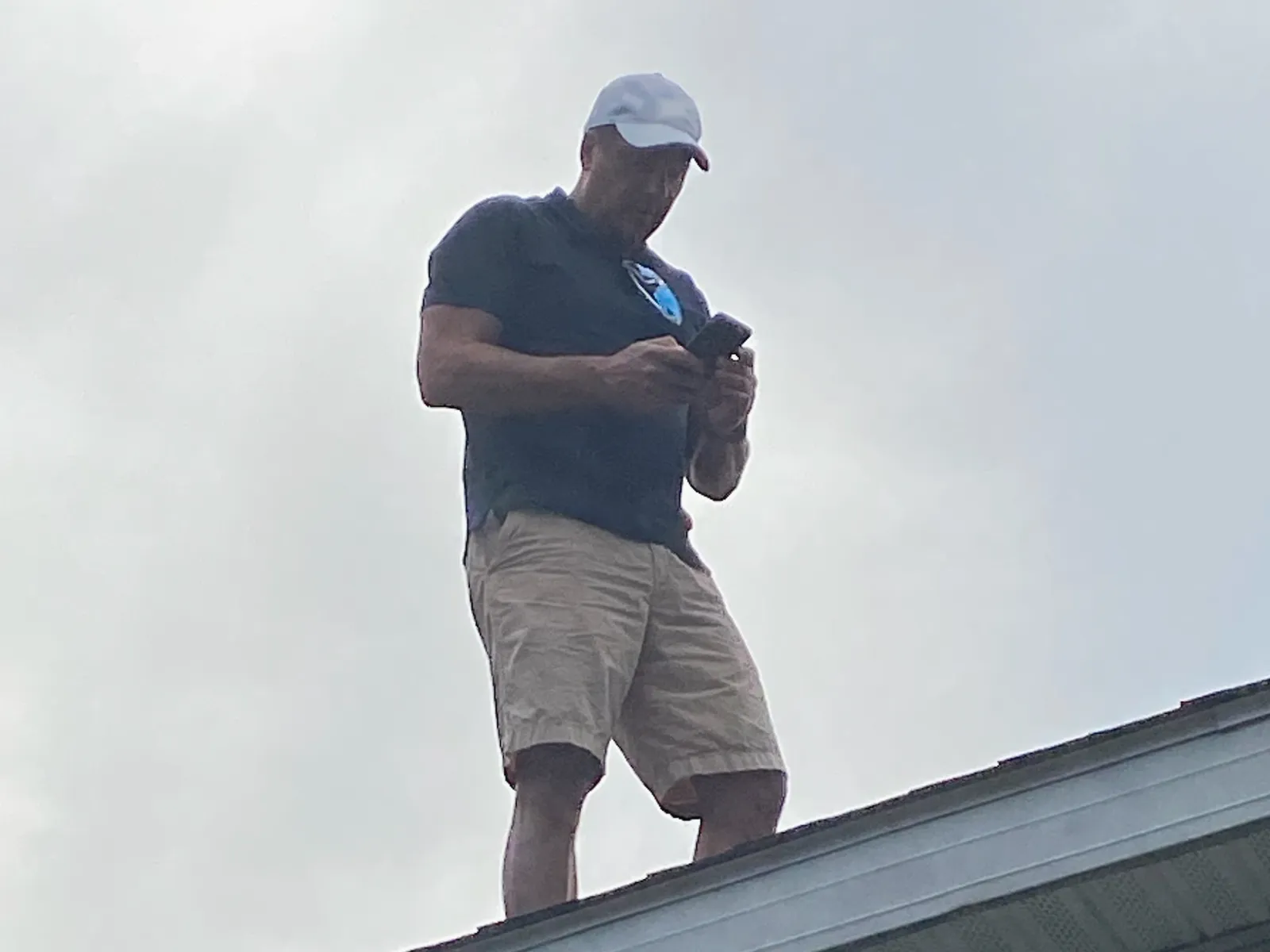 A roofer standing on a shingle roof, photographing it with a phone
