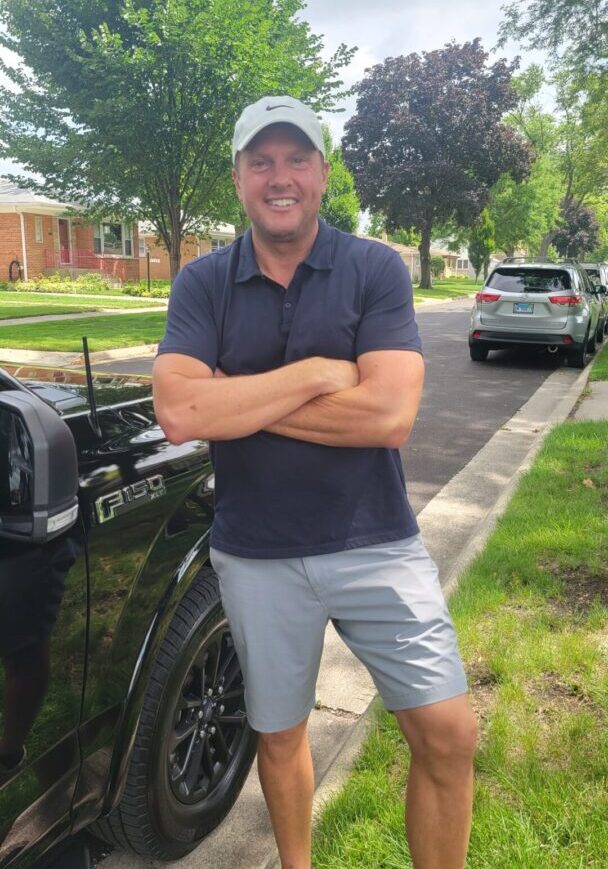 A man standing in front of his car on the street.